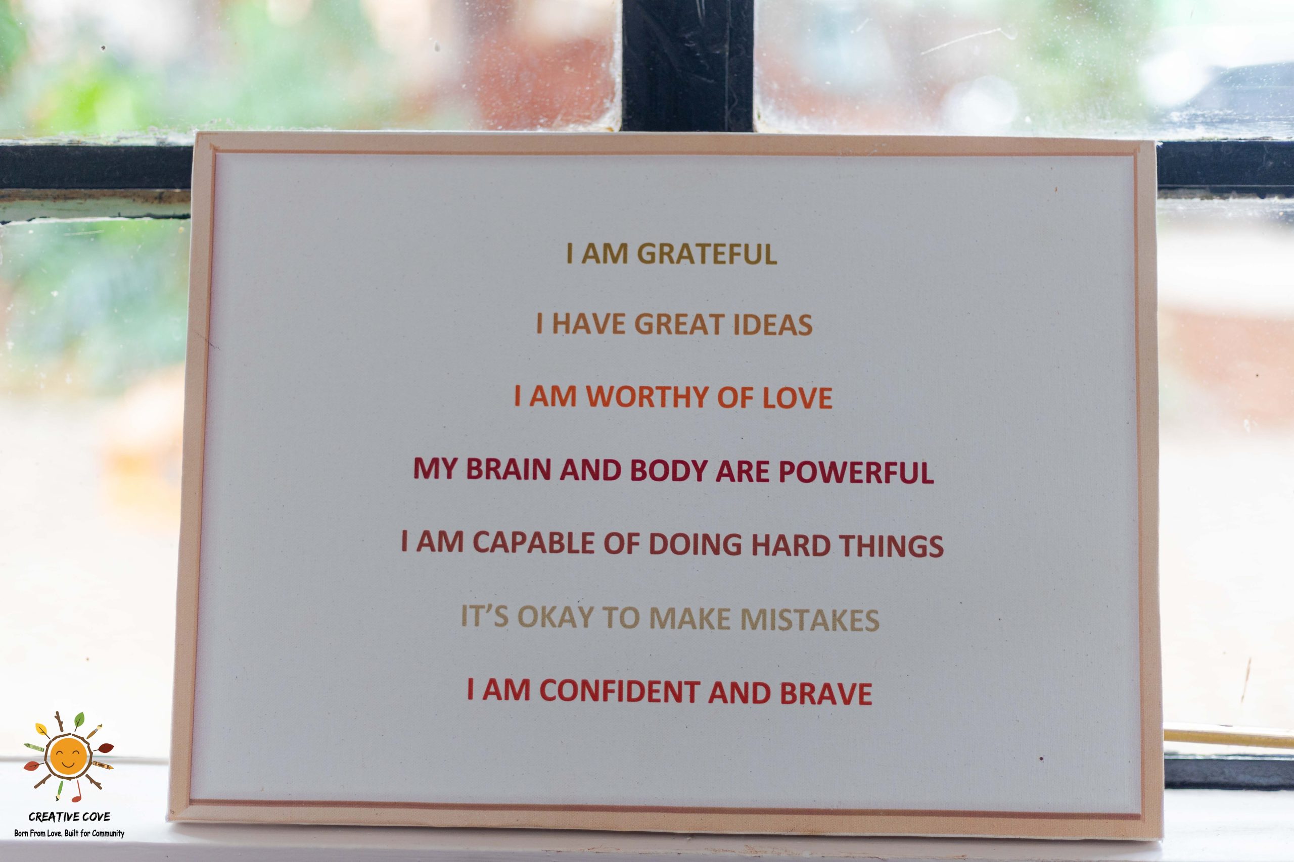 A framed sign of positive affirmations for children displayed by a classroom window
