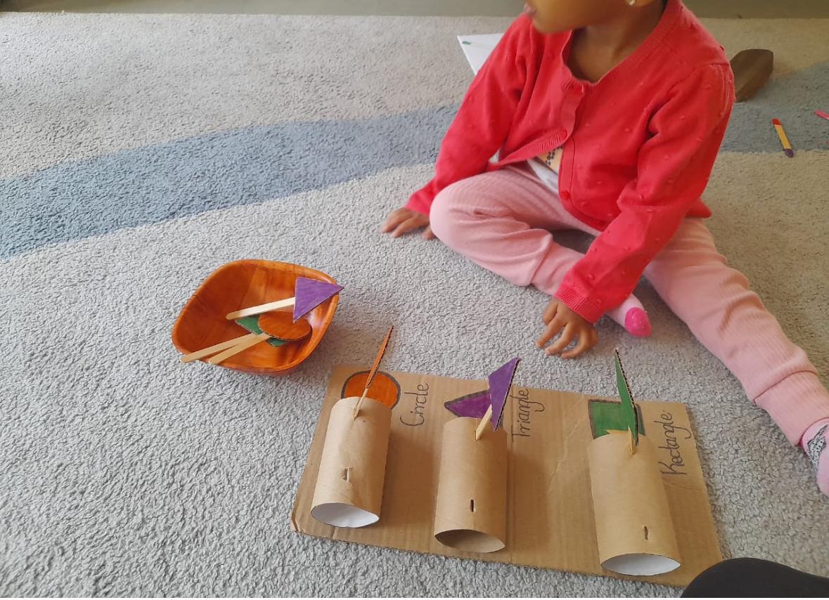 A child matching shapes onto a handmade cardboard sorting board