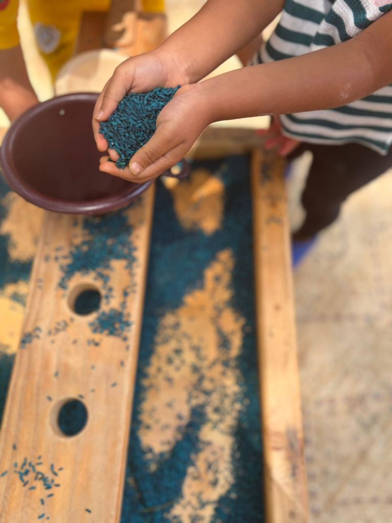 Child scooping colored sensory rice at a sand table