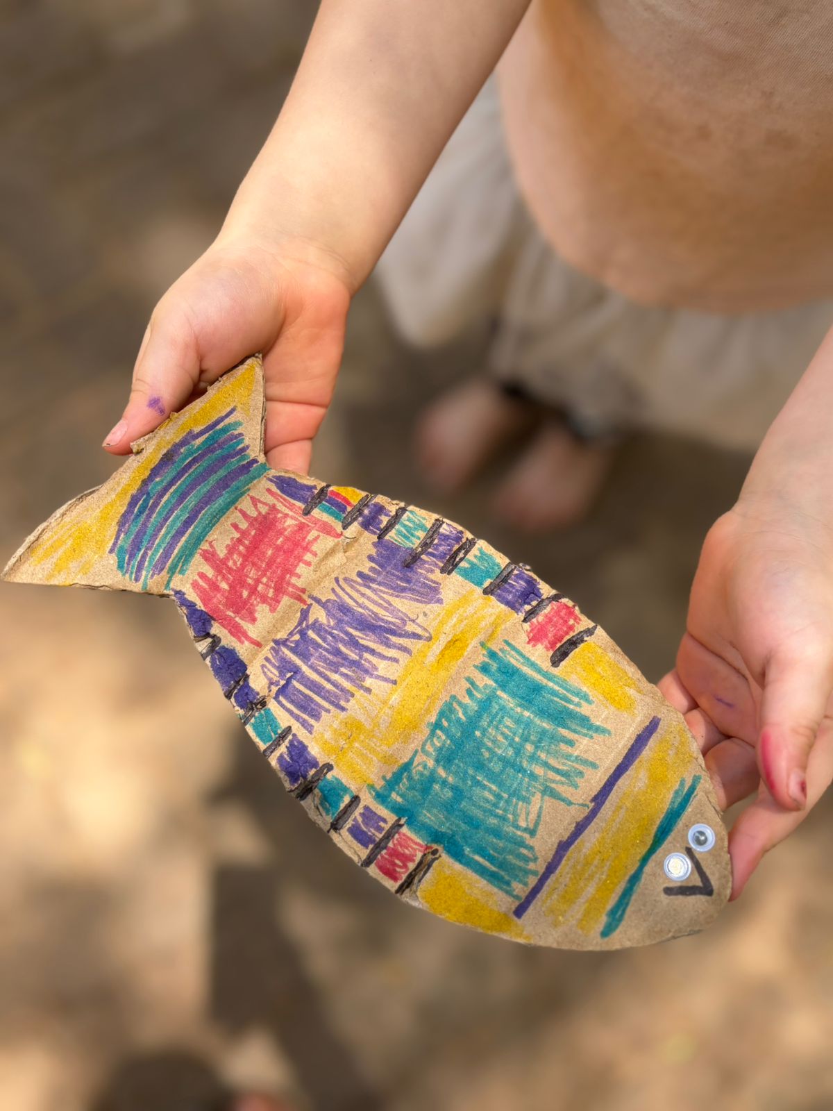 A child proudly holding a hand-painted cardboard fish craft