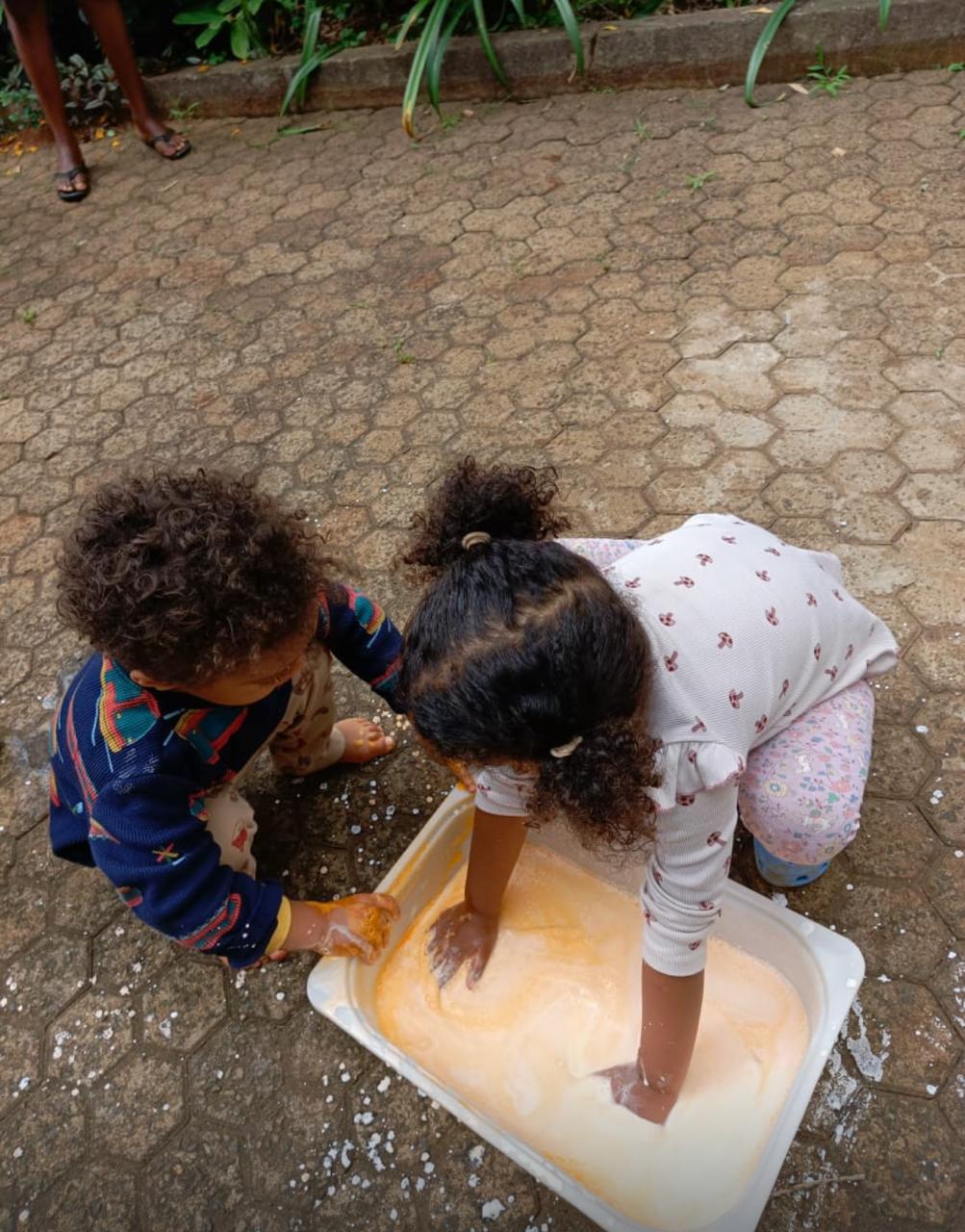 Two children playing together over a sensory bowl, heads bent in focus